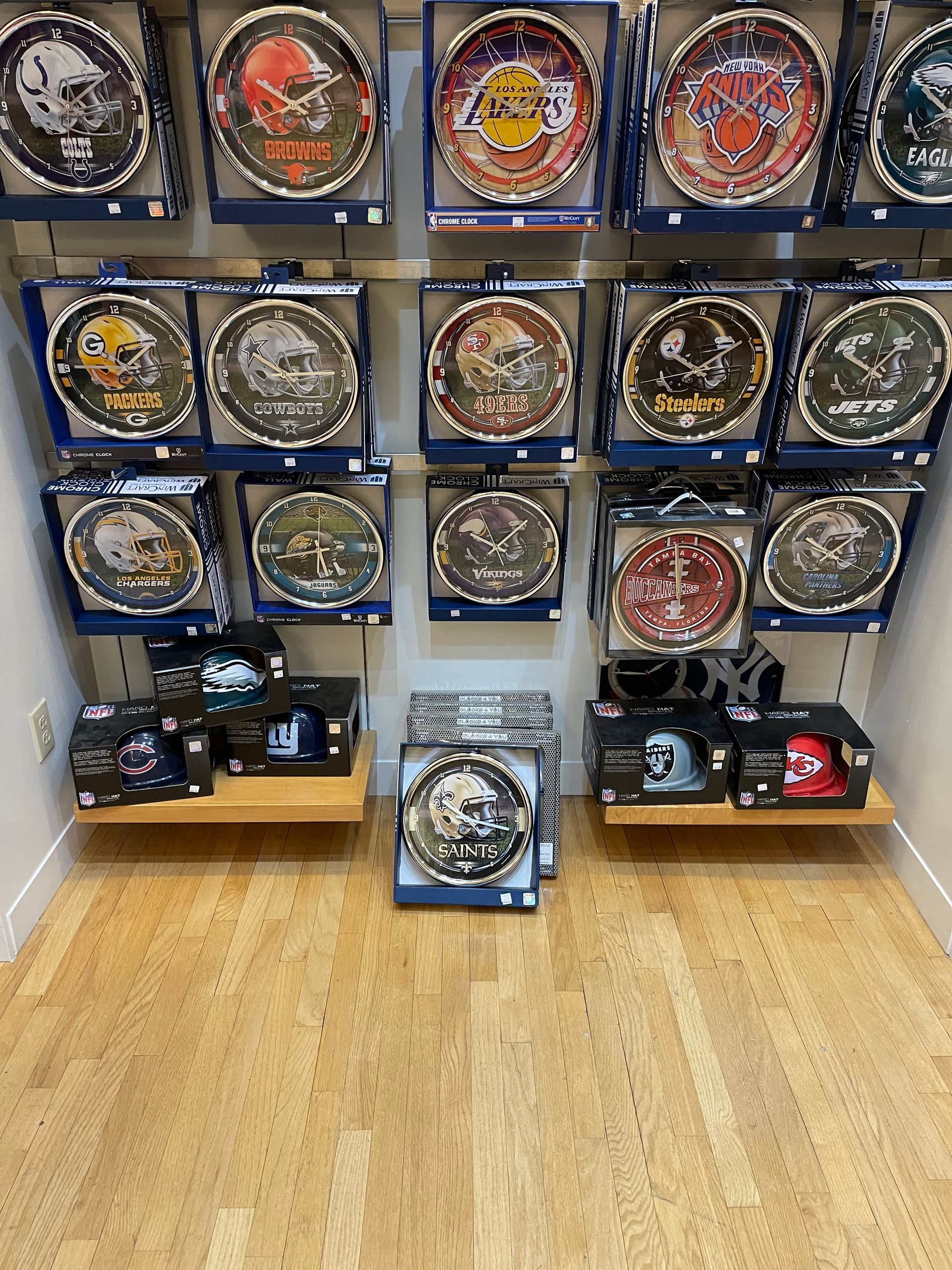 Retail display of NFL team-branded wall clocks in packaging, arranged on shelves inside a store.
