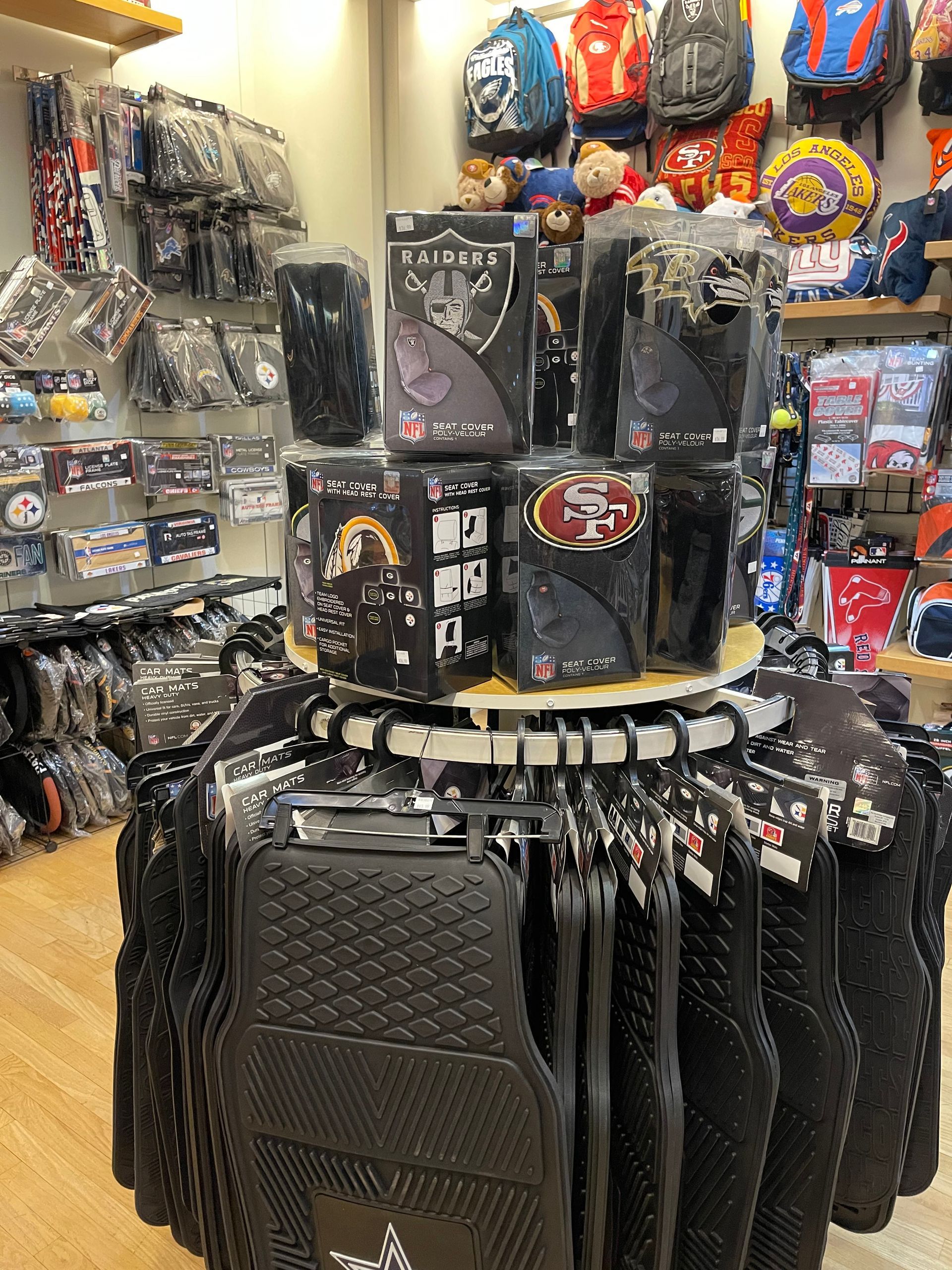 A store display featuring hanging black car floor mats in the foreground with sports-themed merchandise on shelves above.