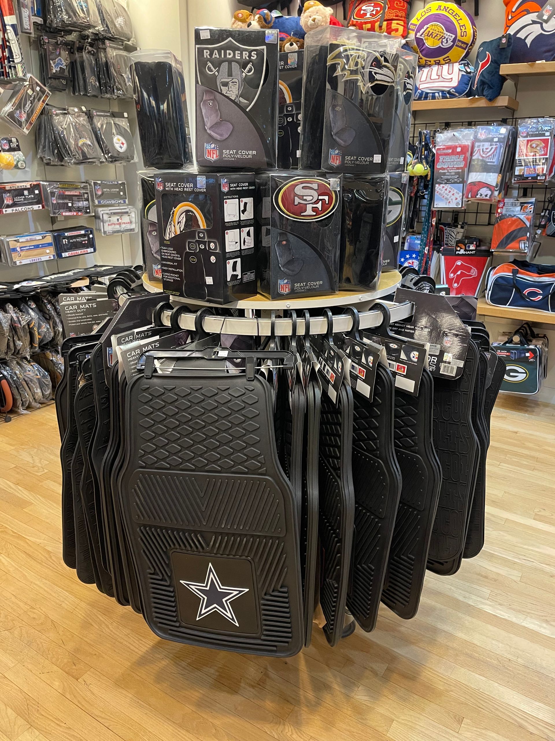 A circular retail display rack filled with black rubber car floor mats featuring various NFL team logos.