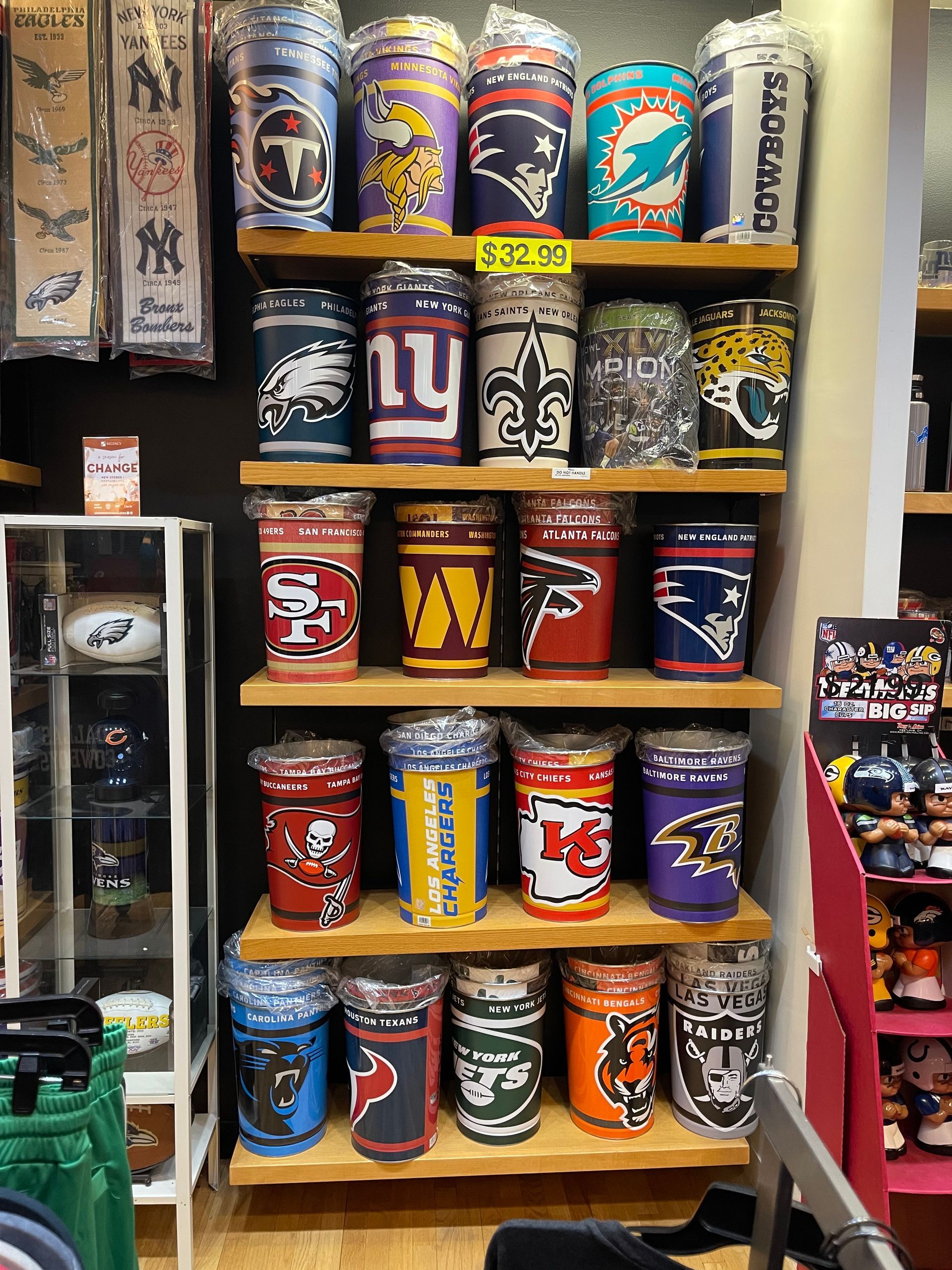 Shelves in a store display various NFL team-themed insulated tumblers, each featuring team colors and logos.
