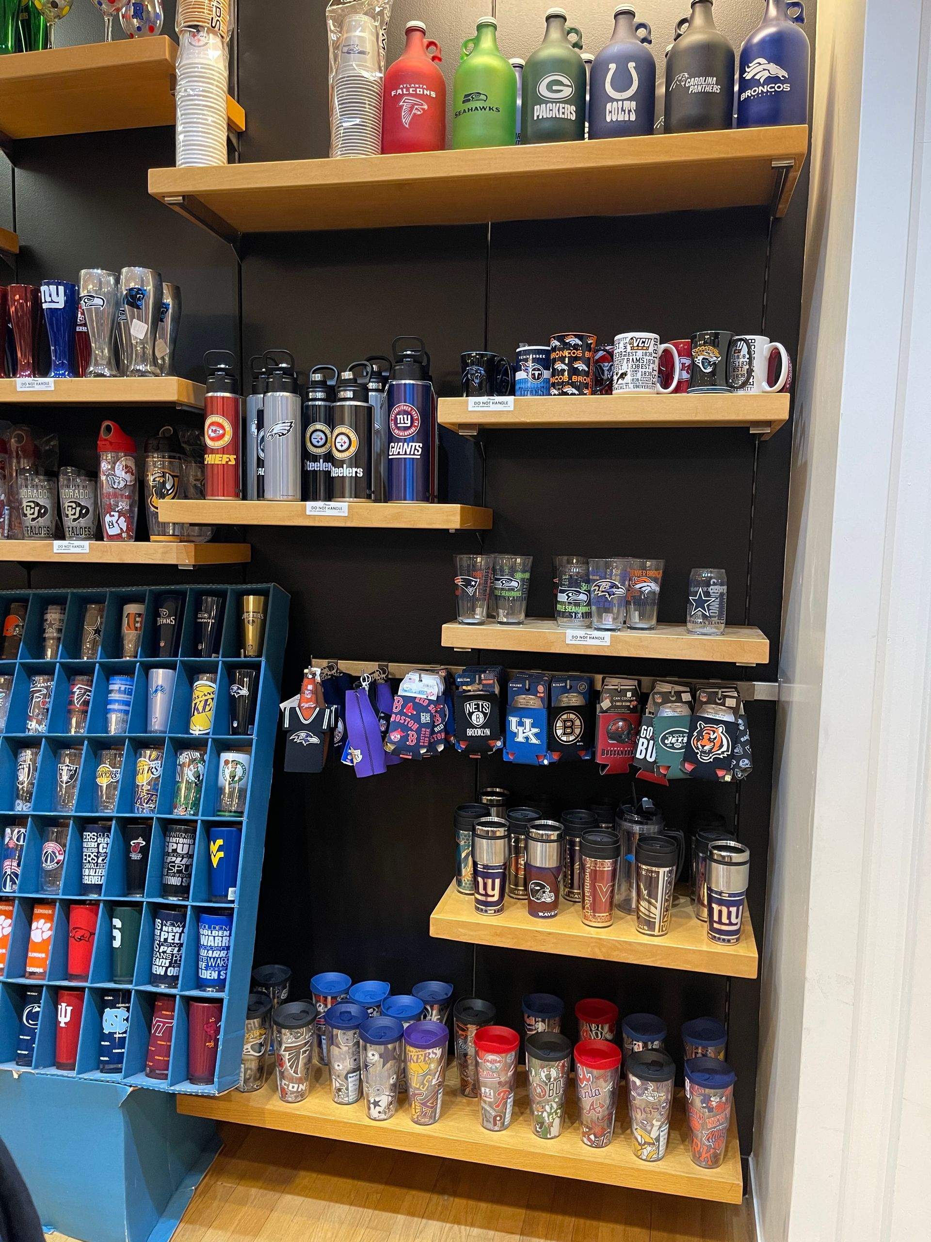 Shelves filled with various sports-themed drinkware, including mugs, tumblers, and bottles, in a retail store.