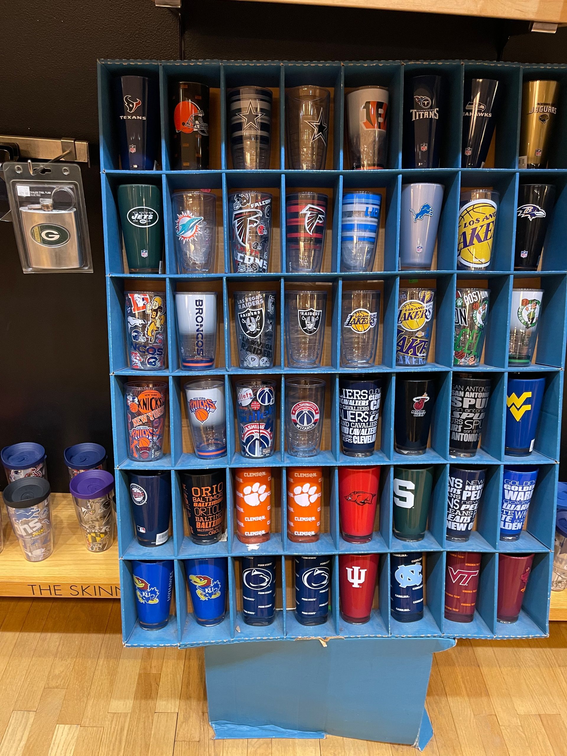 A display rack filled with various collegiate and sports-themed tumblers, organized in rows and columns on shelves.