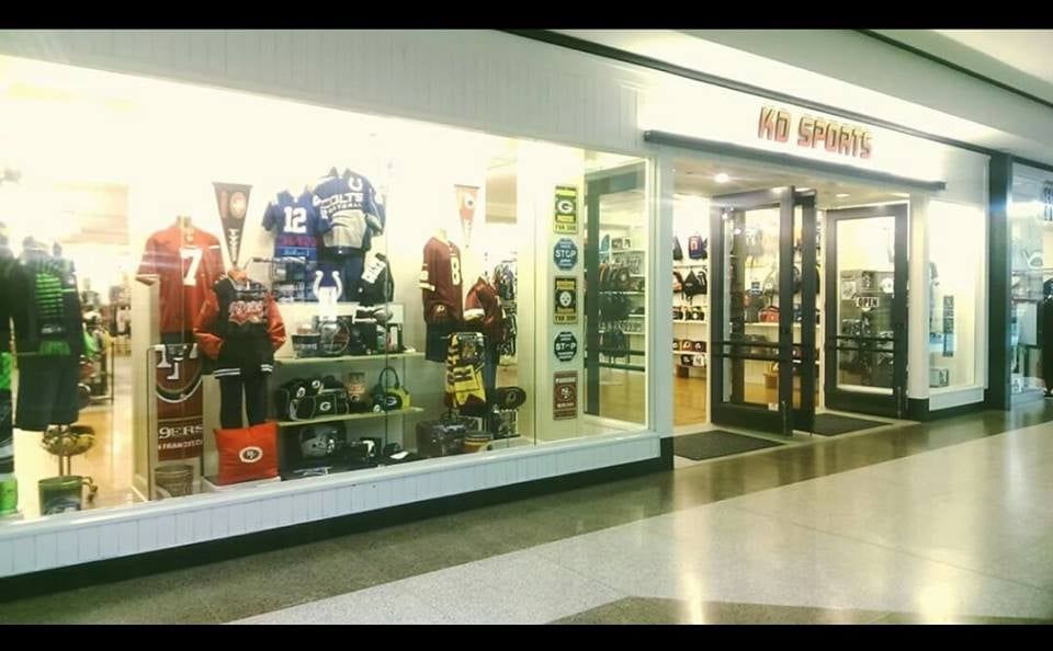 A retail storefront named KB Sports, featuring sports jerseys and merchandise displayed in its window in a mall corridor.