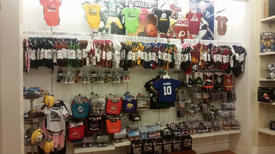 Retail shelf display of various NFL and college team sports merchandise, including baby onesies, bibs, and socks.