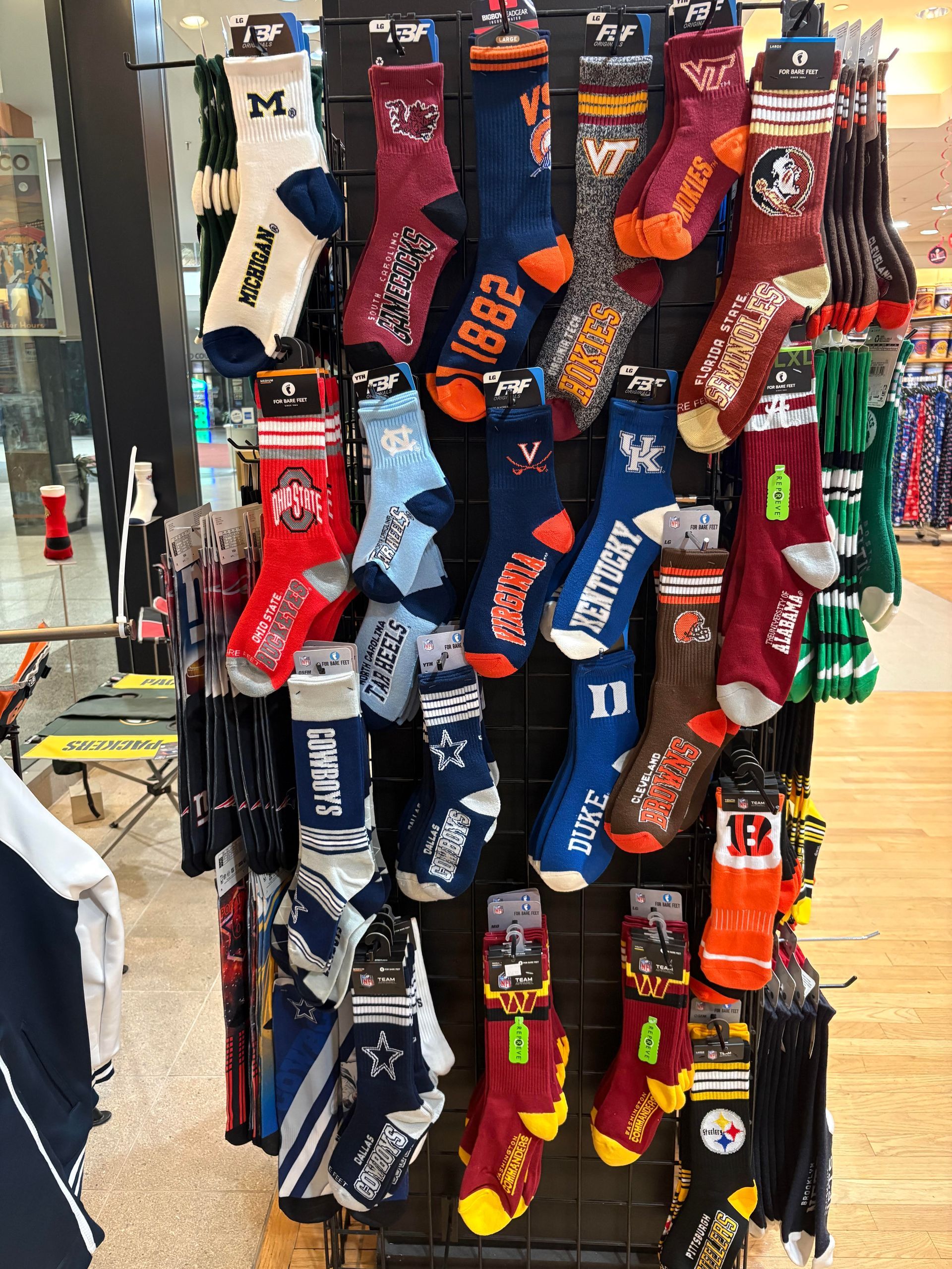 A store display rack filled with various colorful athletic crew socks featuring university and professional sports logos.