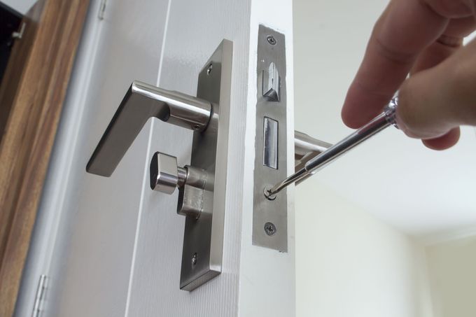 A person is fixing a door handle with a screwdriver.