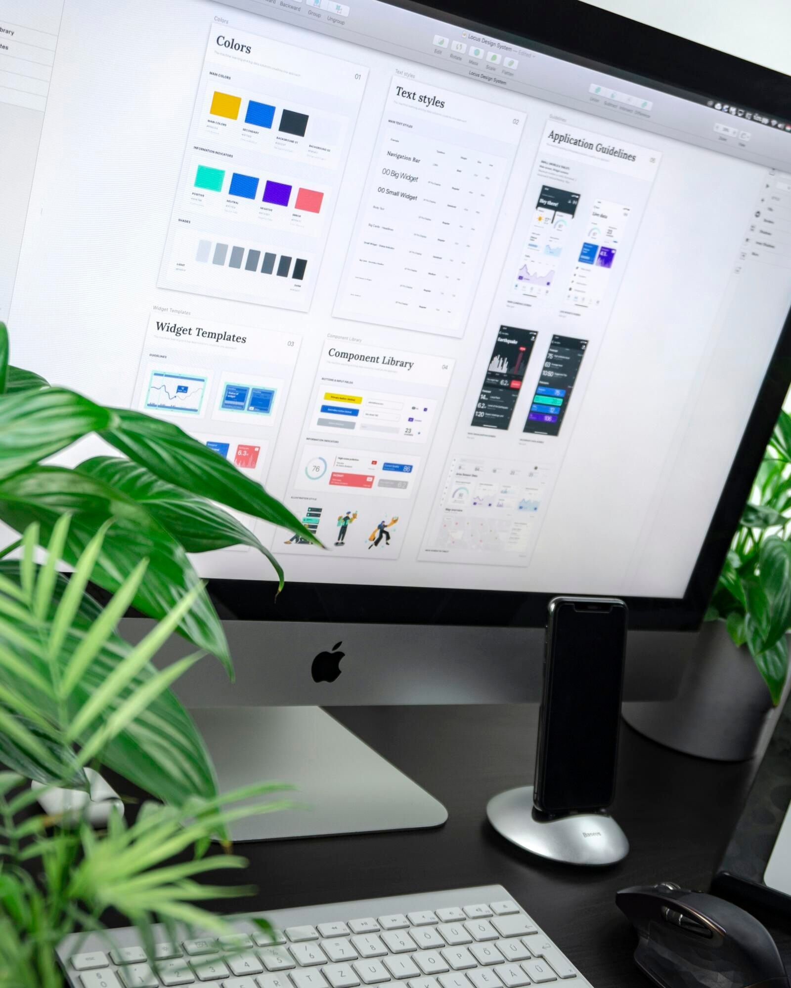 Desktop computer with a design interface, keyboard, mouse, and plants.