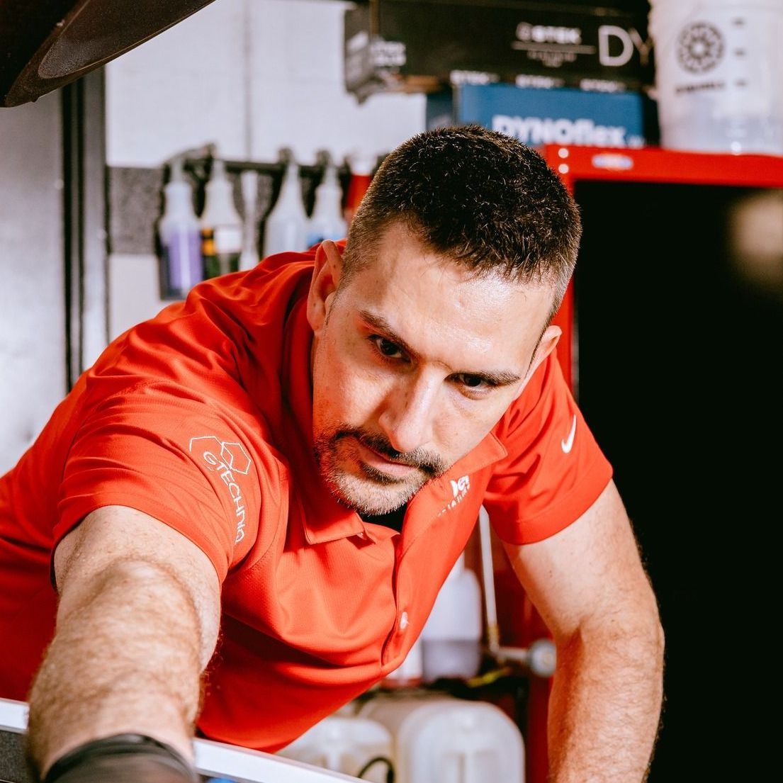 A man in a red shirt is working on a car in a garage.