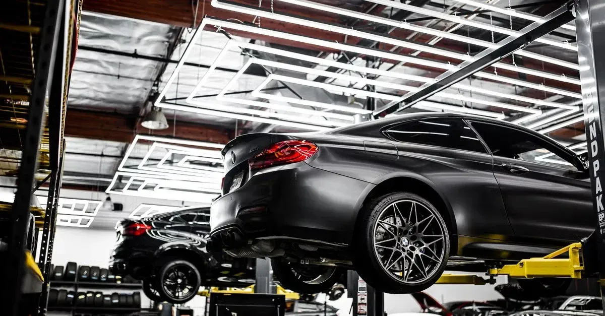 Black car elevated on yellow lift in professional automotive repair shop with industrial ceiling.