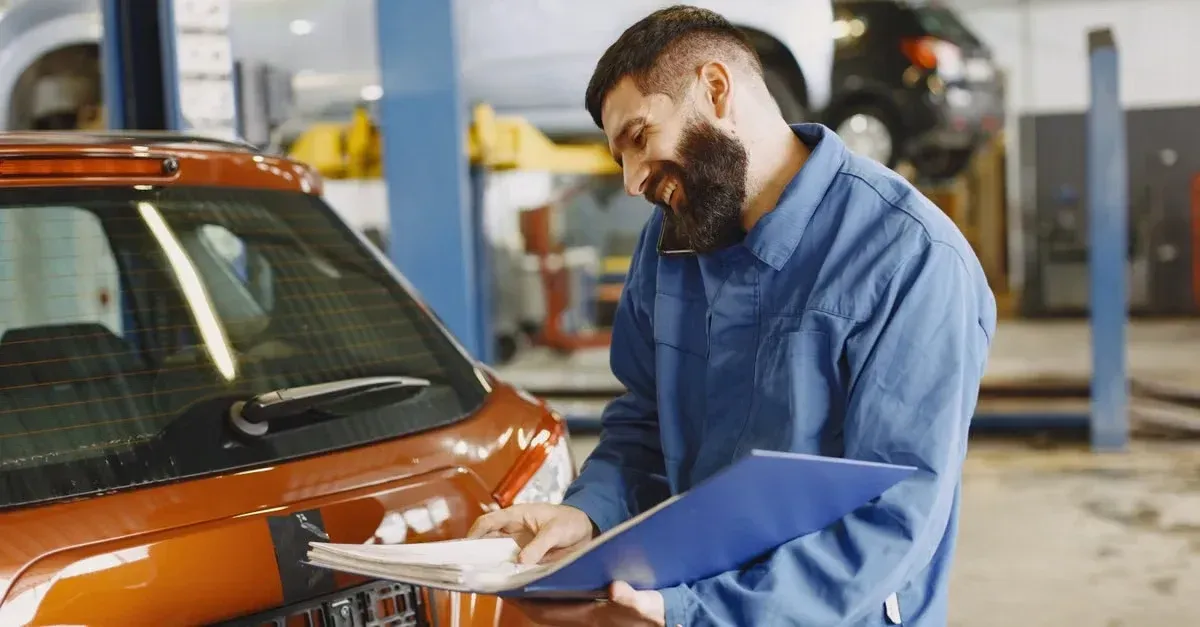 Mechanic documenting automotive SEO results on clipboard while inspecting orange car in service bay.