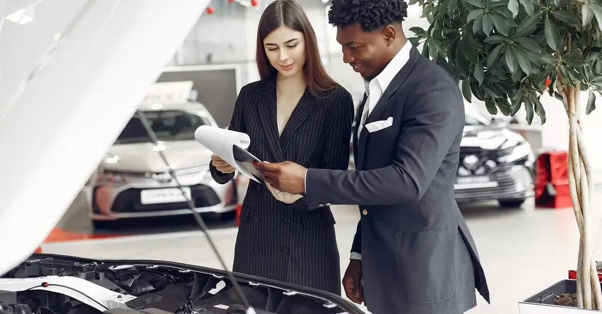 Car salesman showing vehicle details to customer on tablet at dealership showroom.