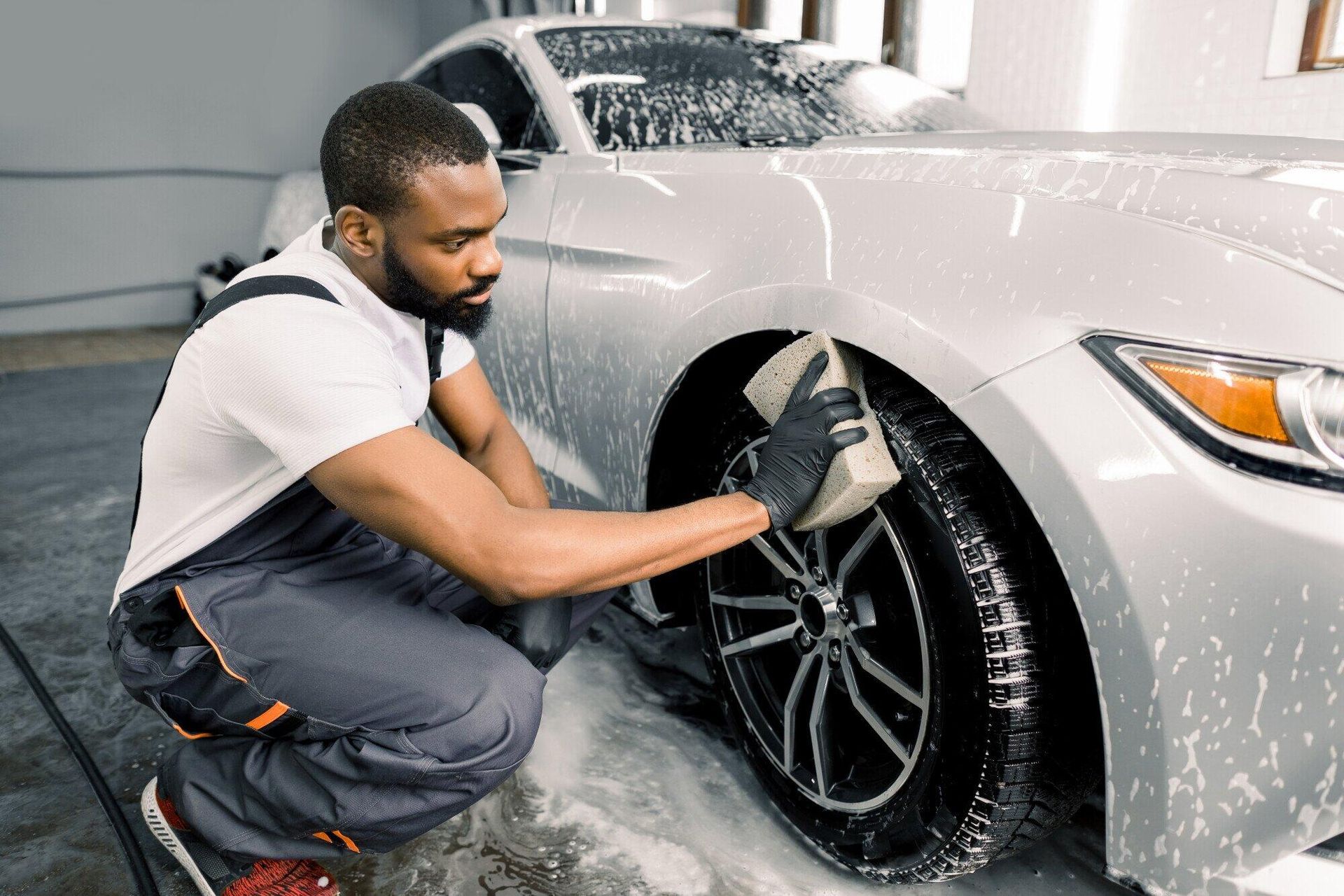 Man washing the tire of a silver car with a sponge in a car wash.