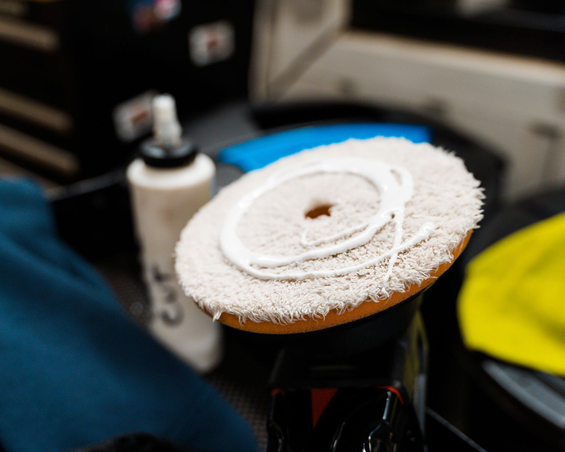White polishing pad with compound on a black machine, ready for car detailing.