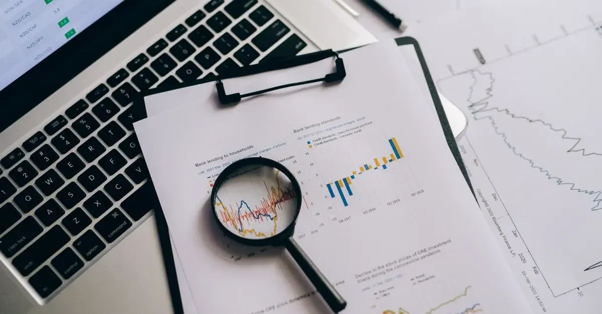 Laptop with magnifying glass over financial charts and graphs showing data analysis and comparison.