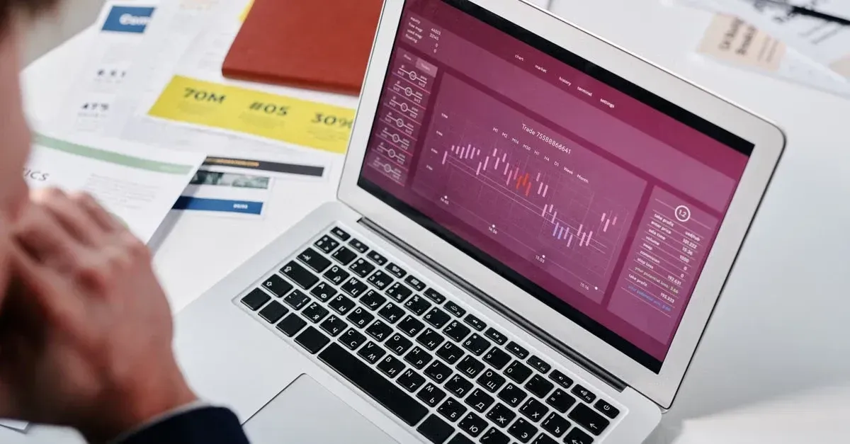 Laptop displaying analytics dashboard with declining charts surrounded by business reports and planning documents.