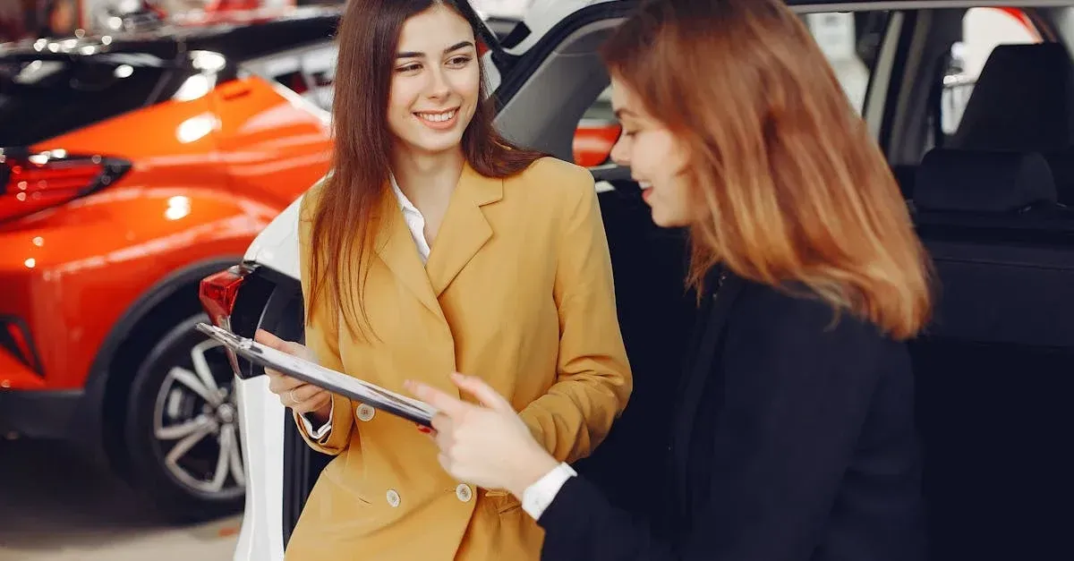 Salesperson in yellow blazer discussing auto detailing leads with customer inside car dealership showroom.