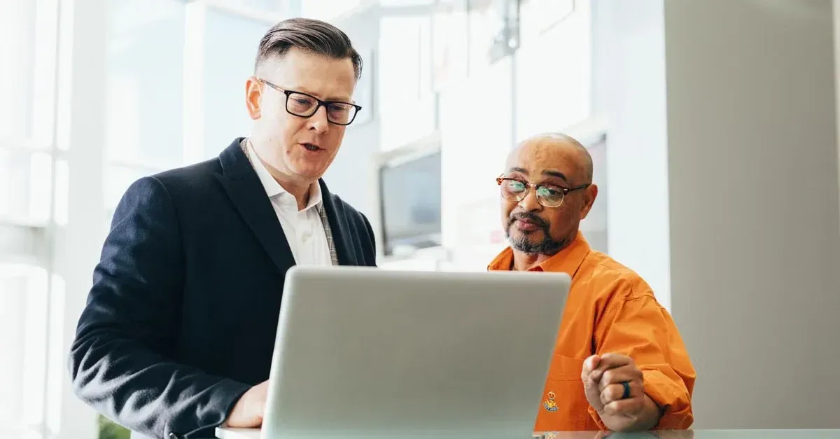 Two professionals discussing CRM automotive industry solutions on laptop in modern office environment.
