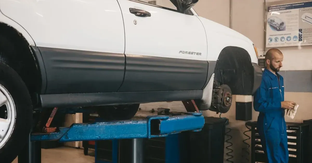 Detailing agency niche technician servicing SUV lifted on blue hydraulic lift in professional shop garage.