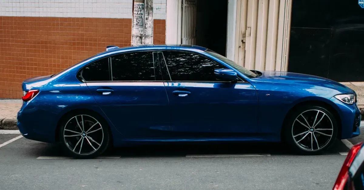 Blue sedan with dark window tint parked on street, showcasing window tint advertising potential.
