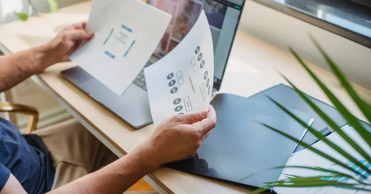 Designer reviewing window tinting website design mockups and layouts on desk with laptop and plant.