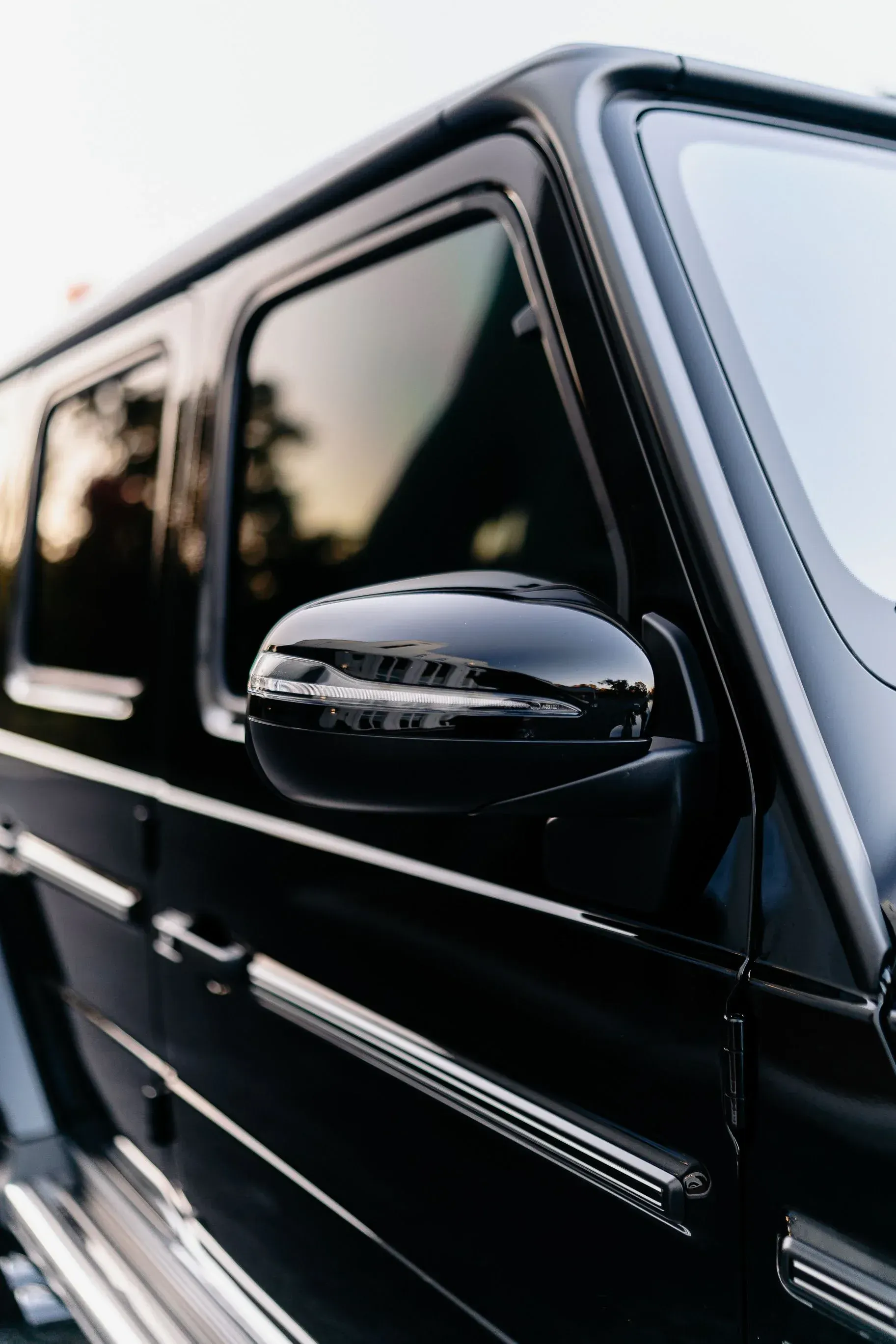 Close-up of a sleek black luxury SUV, highlighting its side mirror and tinted windows. 
