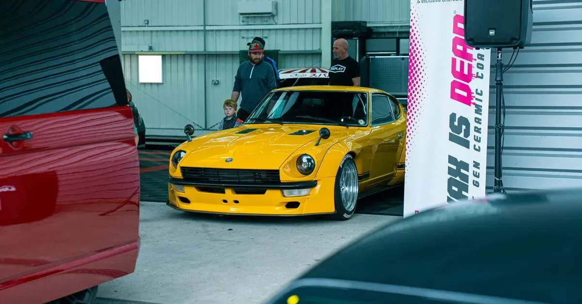 Bright yellow sports car in professional auto detailing garage with technicians inspecting vehicle for detailing leads.