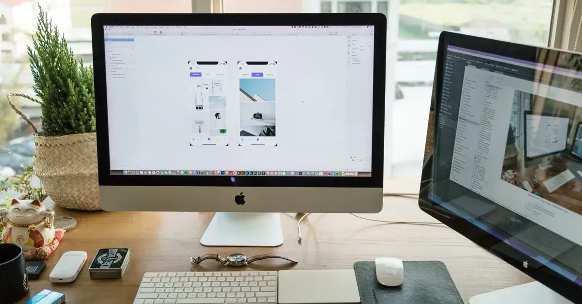 Designer workspace with iMac displaying car detailing website mockup, dual monitors, keyboard, and office plants by window.