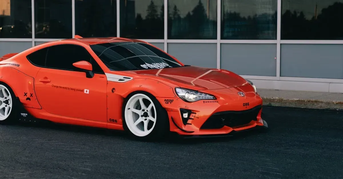 Bright red sports car with dark window tint and white wheels parked against modern building.