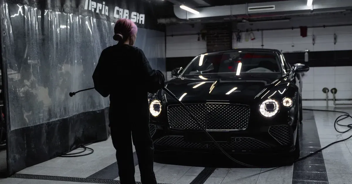 Professional detailer inspecting black luxury car in CRM auto detailing garage with LED lighting.
