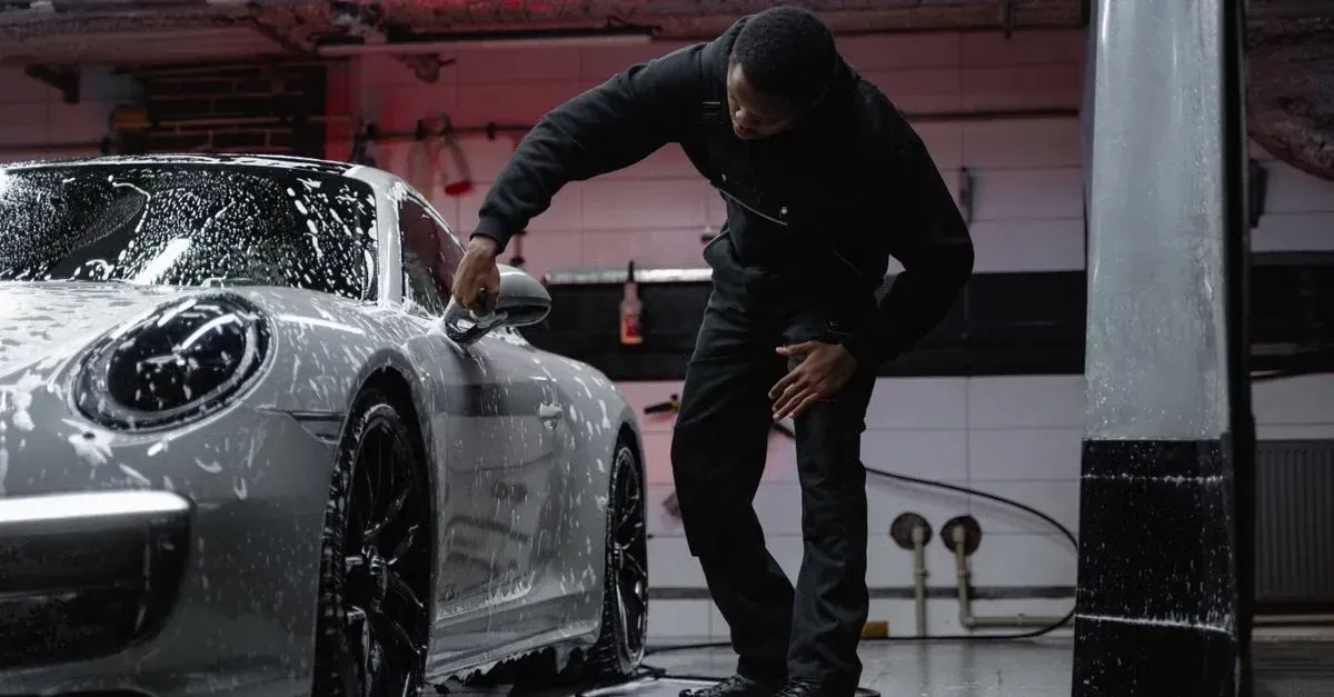 Man washing luxury car with foam and water in professional detailing garage.