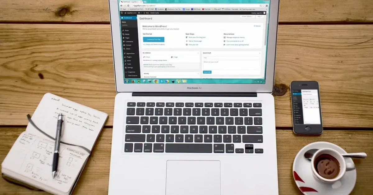 Laptop displaying website dashboard with smartphone, notebook, and coffee on wooden desk workspace.