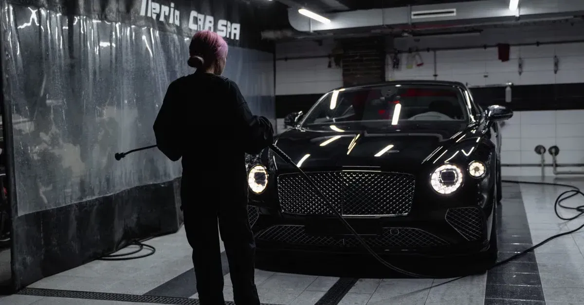 Professional detailer inspecting black luxury car in modern detailing facility with lighting.