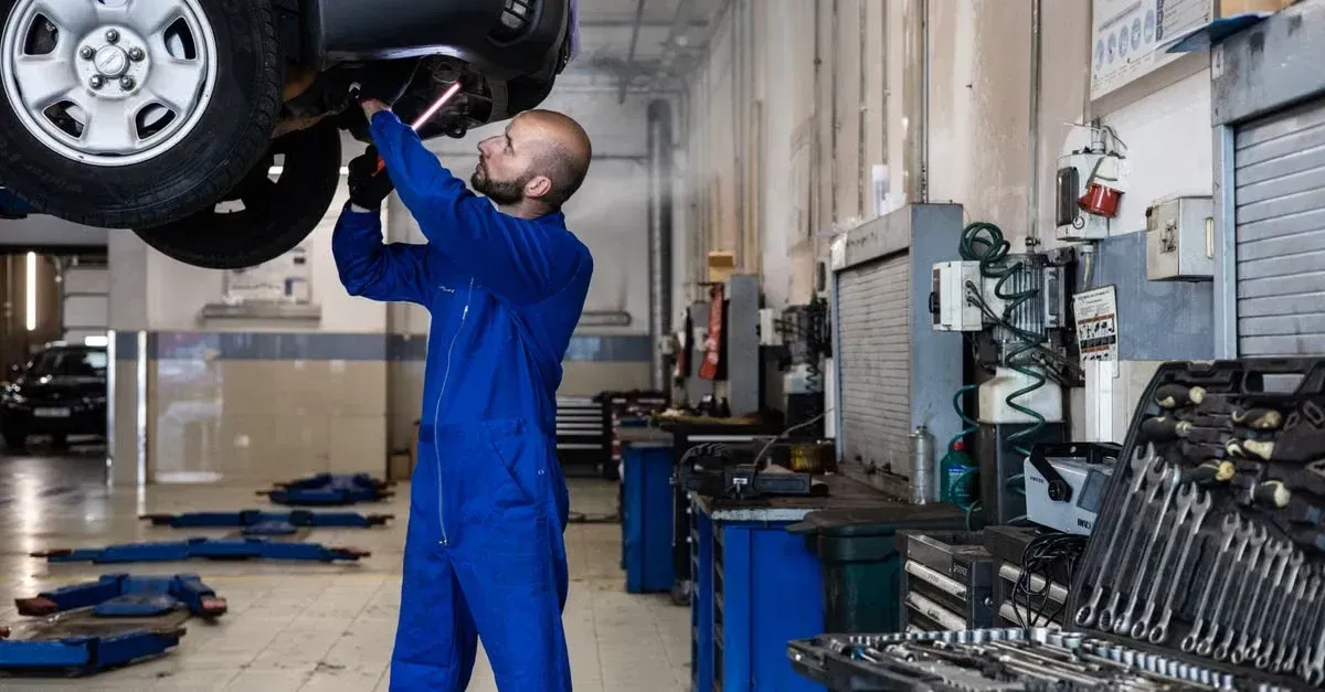 Mechanic in blue uniform inspecting tire in automotive workshop for technical SEO automotive maintenance guide.