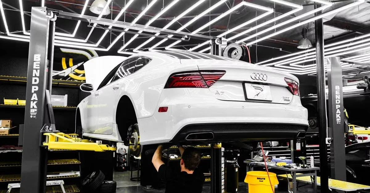 White Audi lifted on yellow hydraulic car detailing business lift in professional garage workshop.