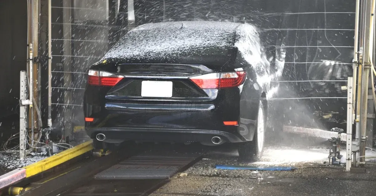 Black sedan receiving high-pressure water spray wash at automated car wash station with professional CRM auto detailing.
