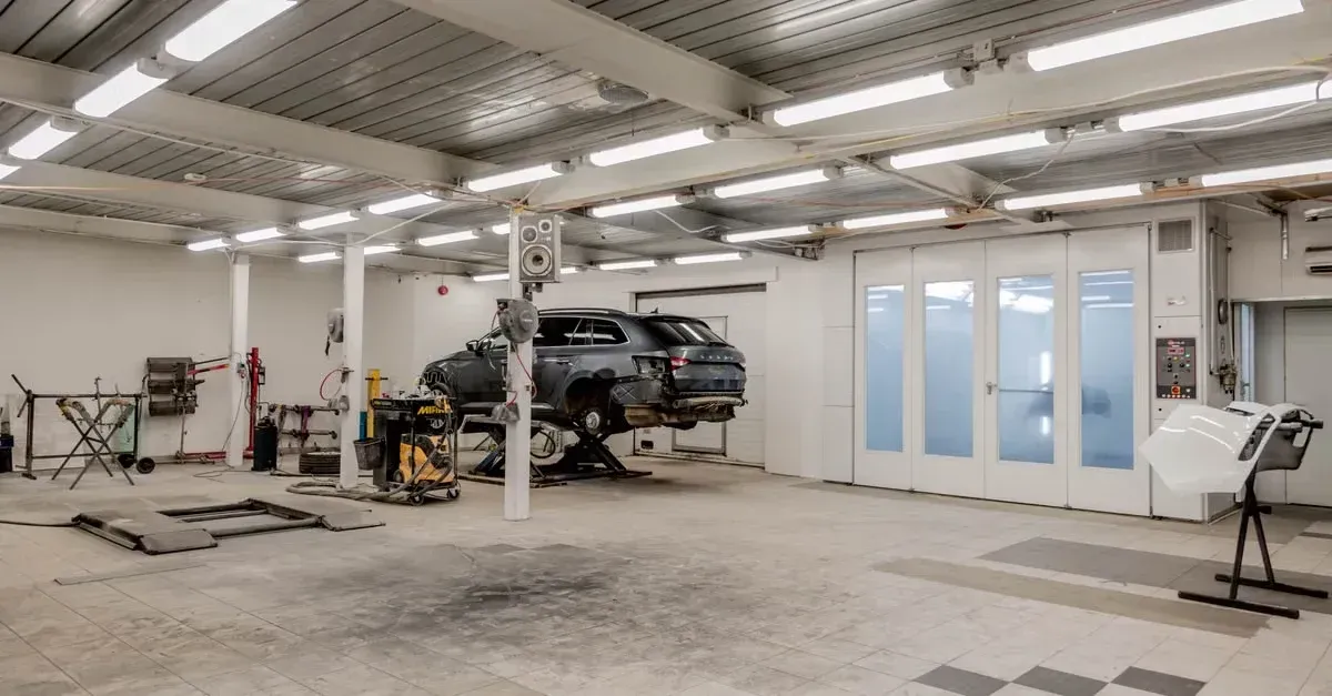 Modern automotive service bay with lifted black vehicle, diagnostic equipment, and bright LED ceiling lighting.