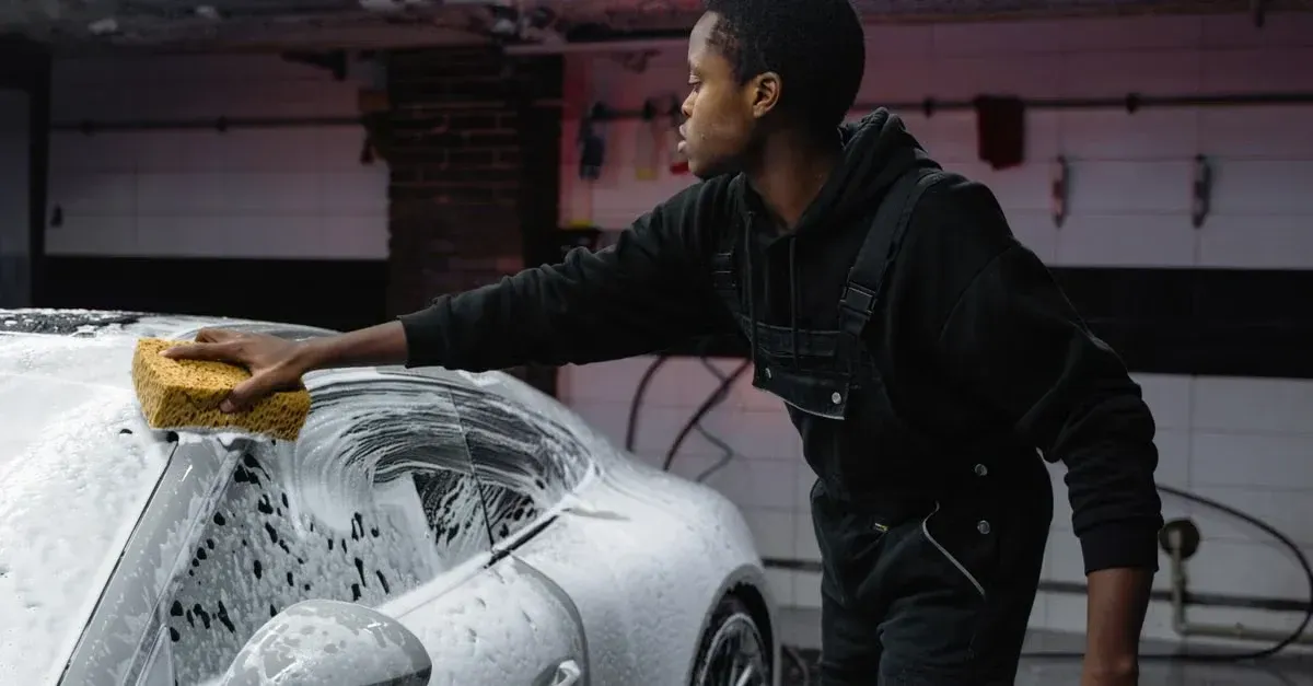 Worker washing white car with soapy sponge in garage using professional detailing techniques for ROI.