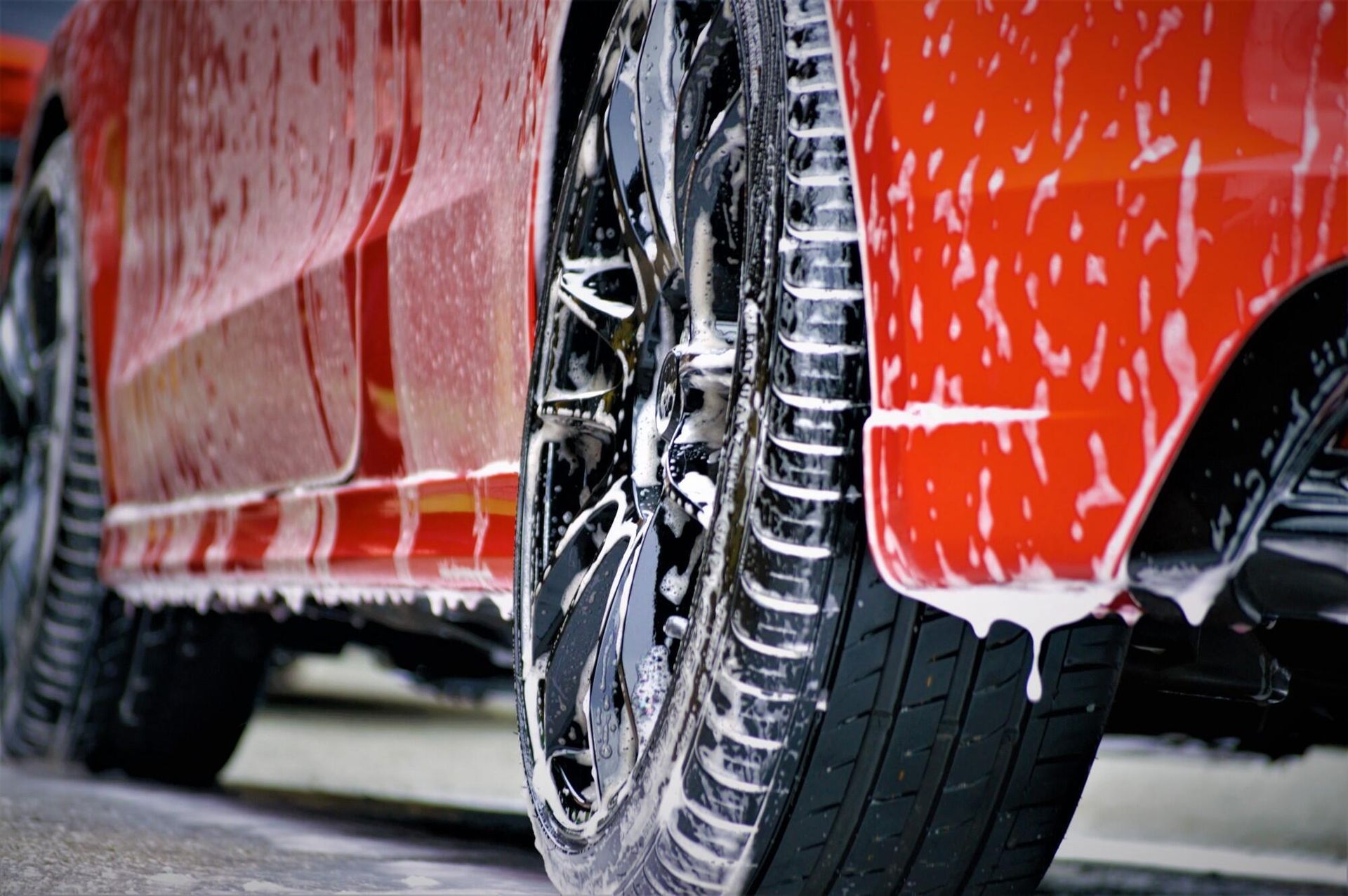 Red car being washed with soapy water, focus on the tire and wheel.