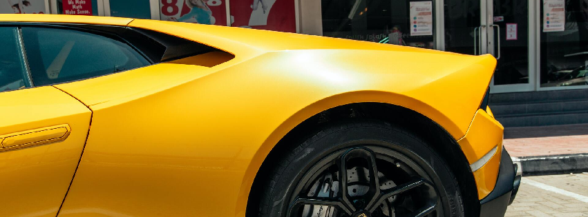 A yellow sports car is parked in a parking lot in front of a building.
