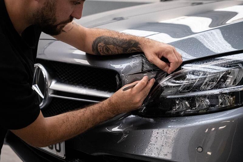 Man applying protective film to car headlight.