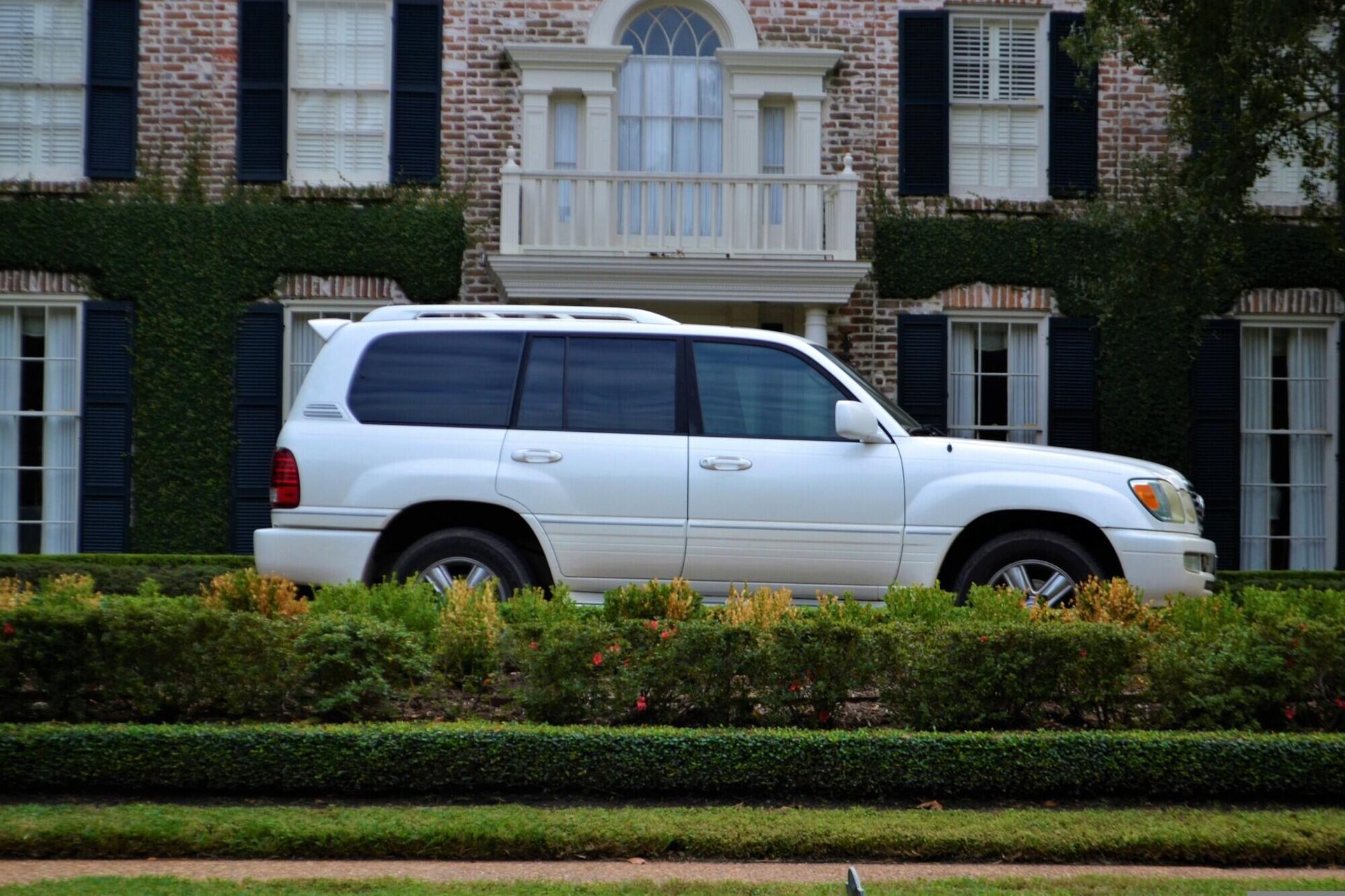 White SUV parked in front of a brick house with dark shutters.