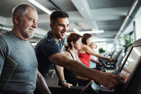 People using treadmills in a bright gym, with one man adjusting the console.