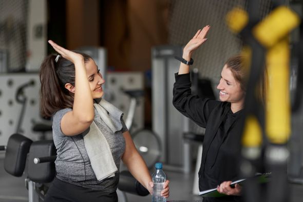 Two people in a gym give each other a high-five, one holding a water bottle.