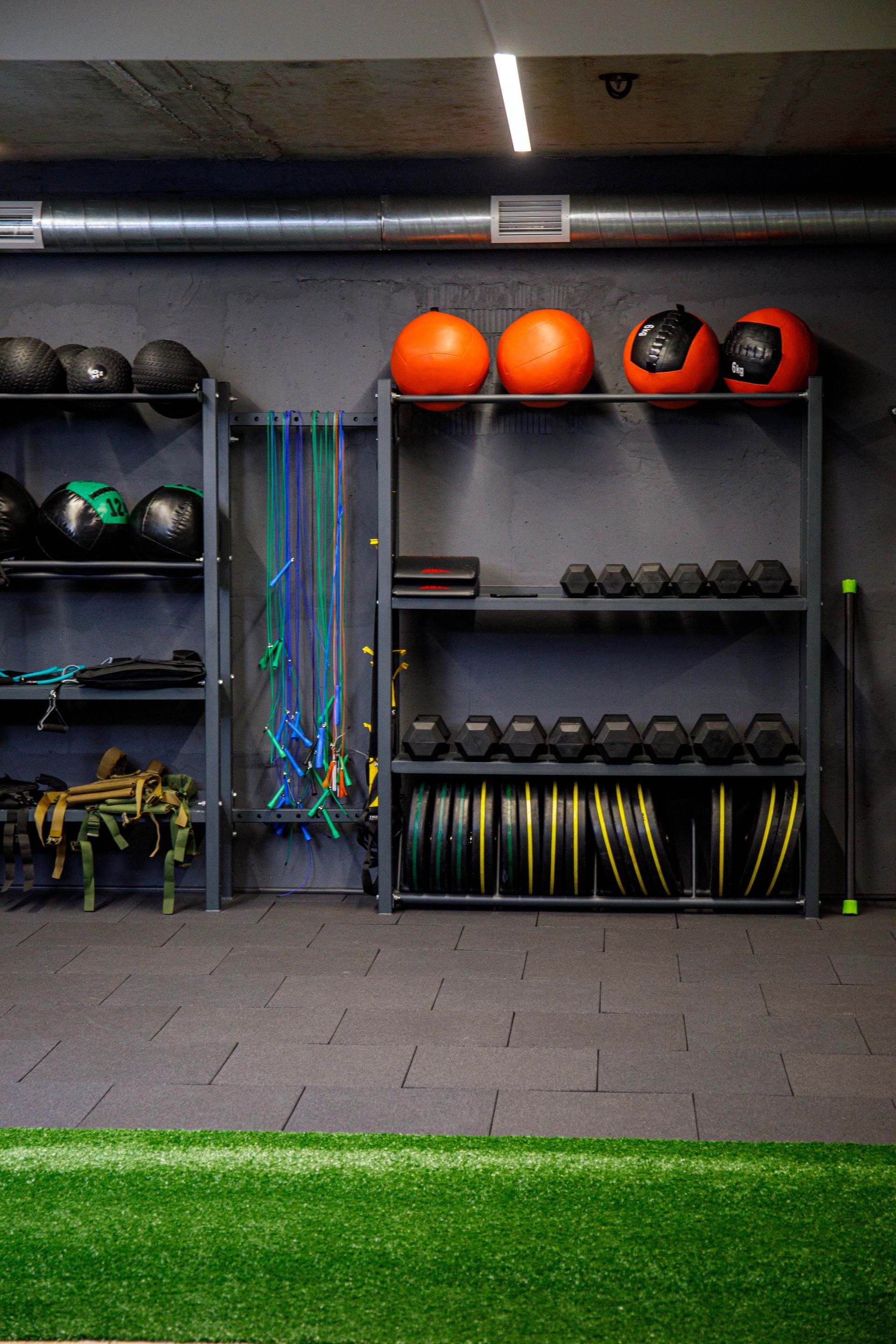 Gym storage shelves with medicine balls, kettlebells, resistance bands, and turf flooring