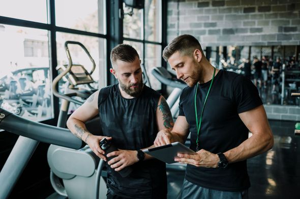 Two men reviewing a tablet in a gym, with workout equipment in the background