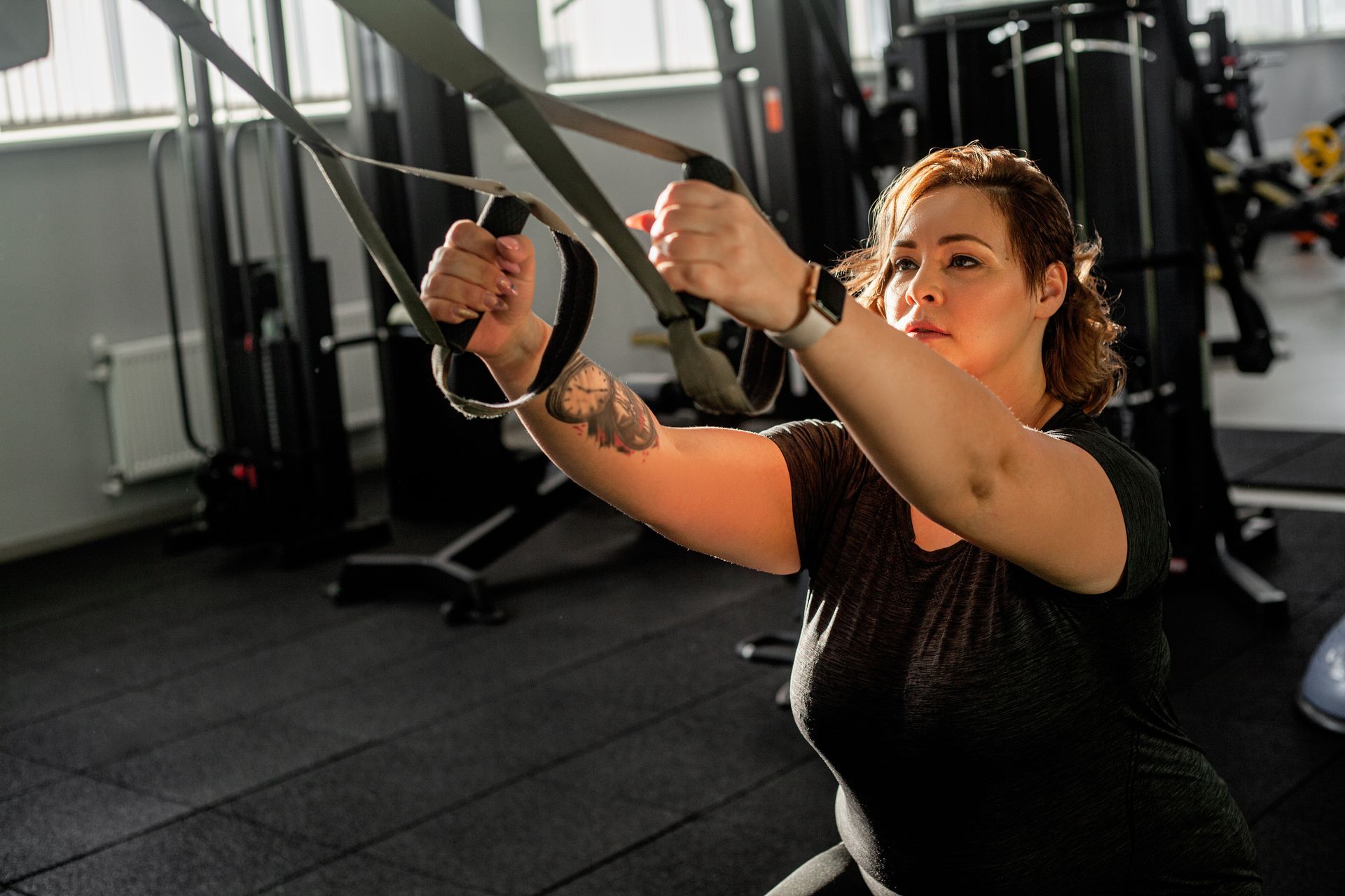 Woman using cable machine in a gym, pulling handles with focused expression