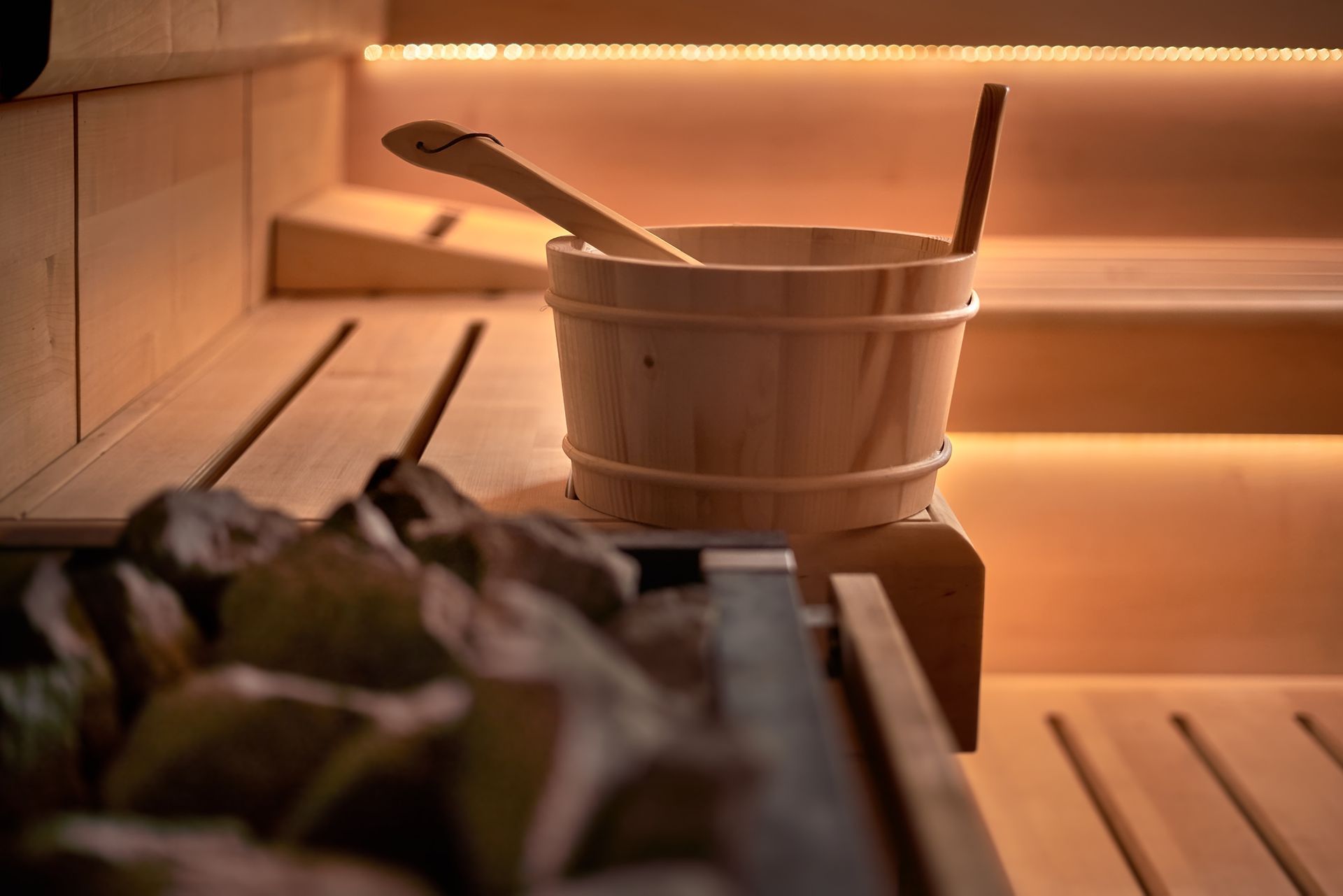 Wooden sauna bench with a bucket, ladle, and towels in warm orange light