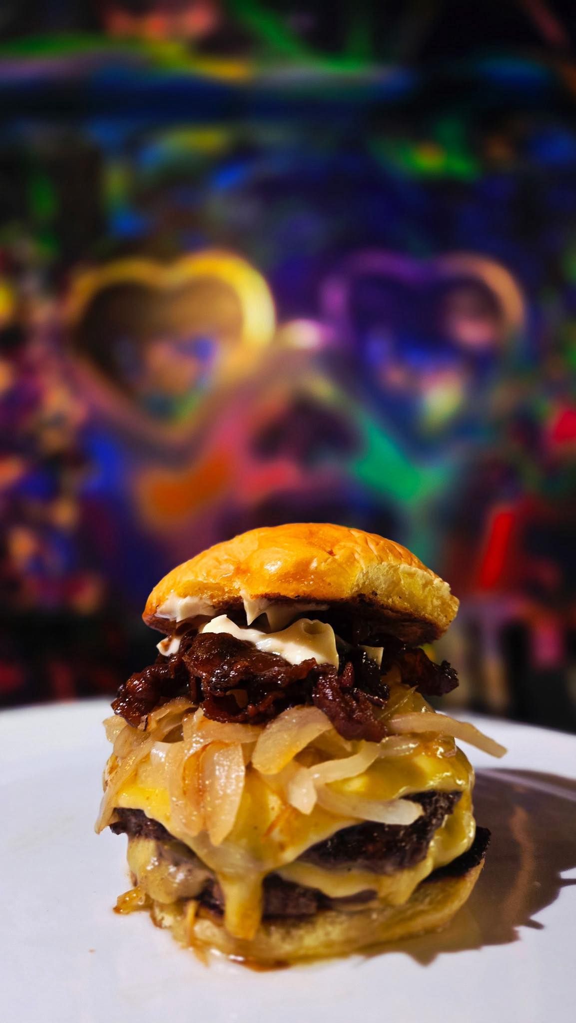 Mini burger with caramelized onions, sauce, and bun, on a white plate, against a colorful backdrop.
