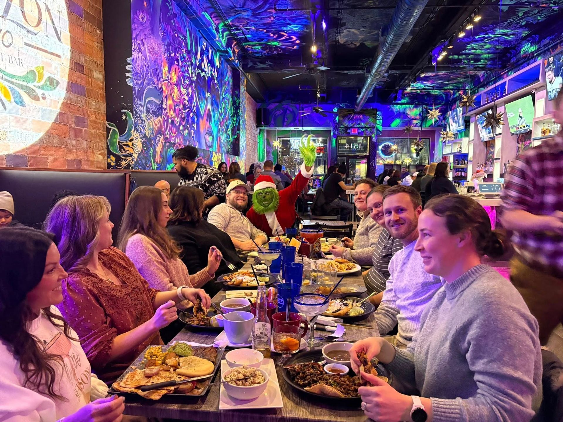 People seated at a table in a brightly lit restaurant, dining and socializing; holiday decorations visible.