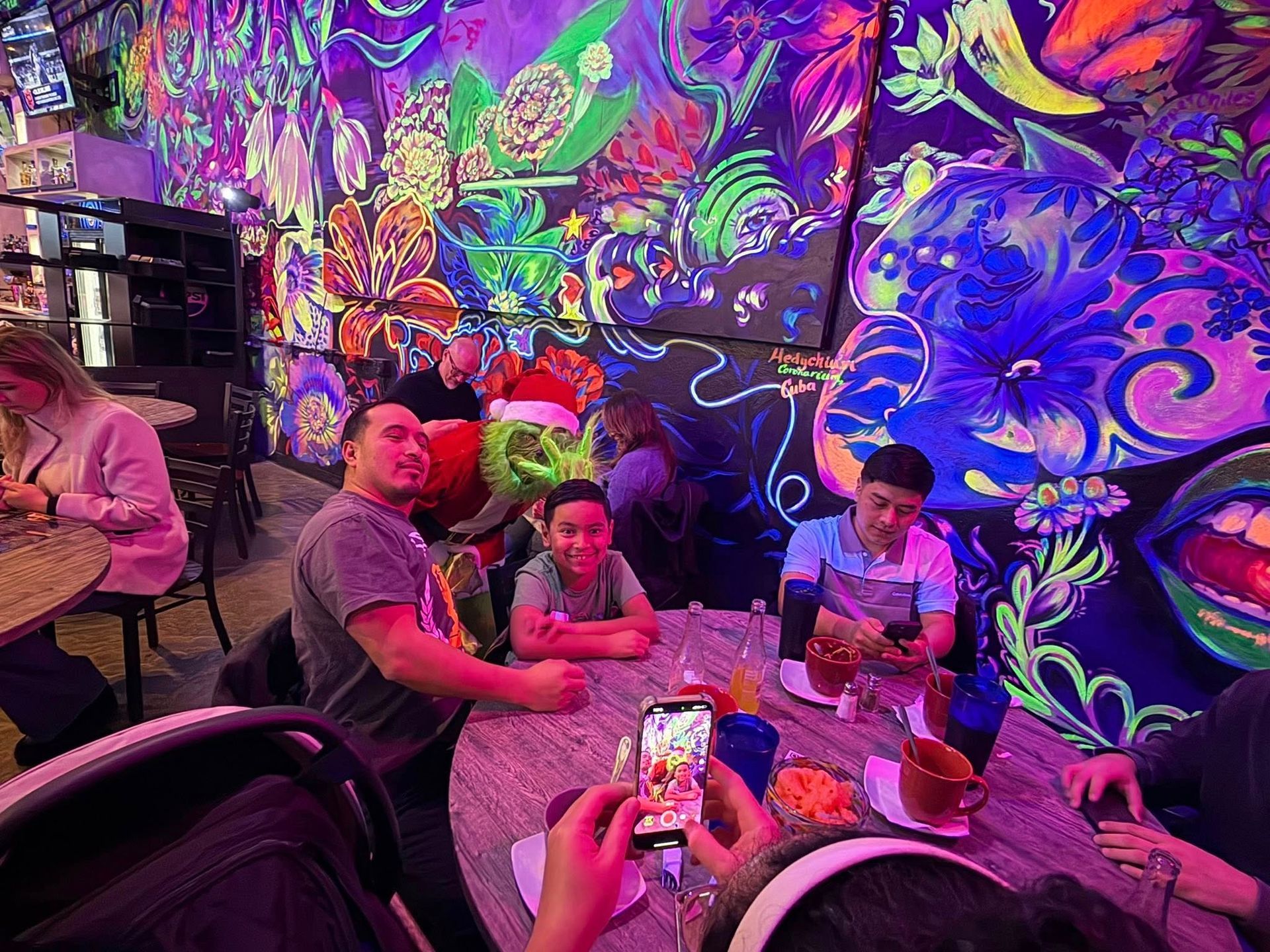 People seated at a table in a brightly painted room with a Grinch character.